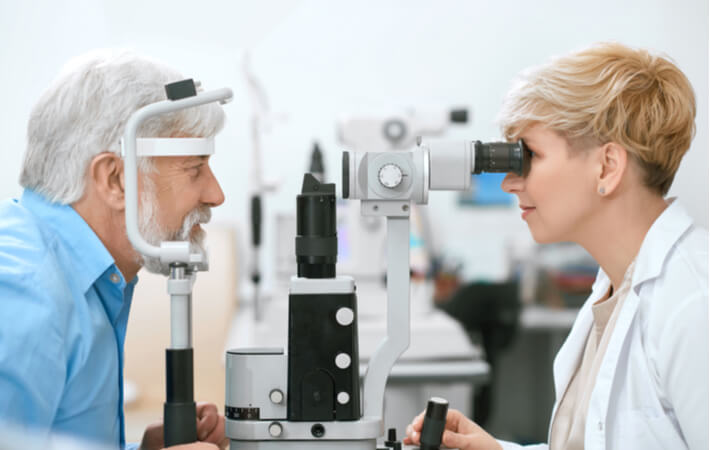 A female optometrist examines an older man's eyes with a tonometer.