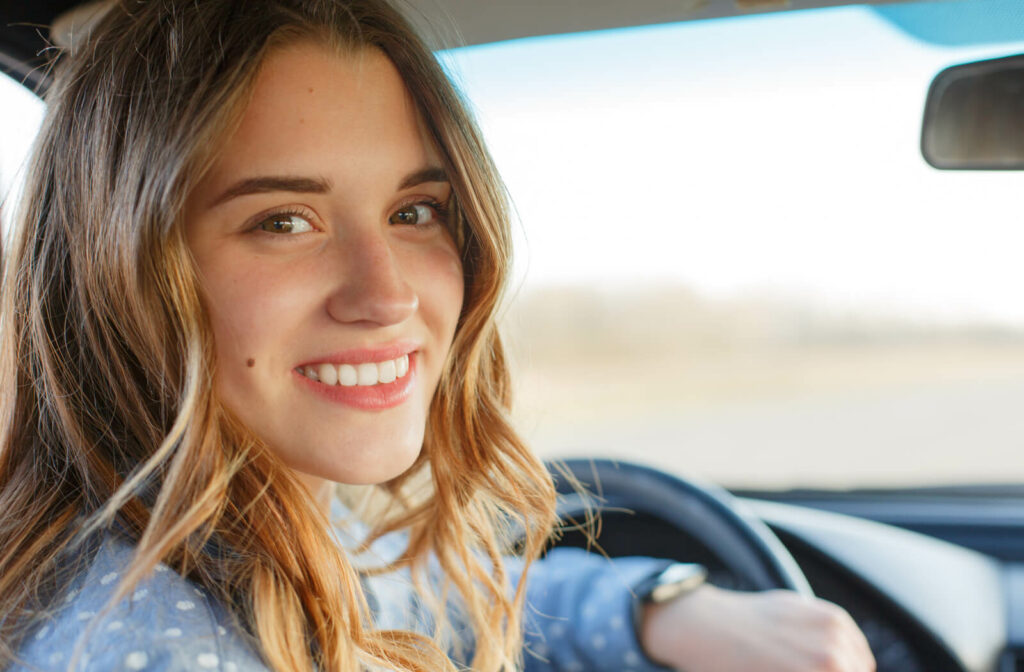 A smiling woman looks back while sitting in the driver's seat of a car.