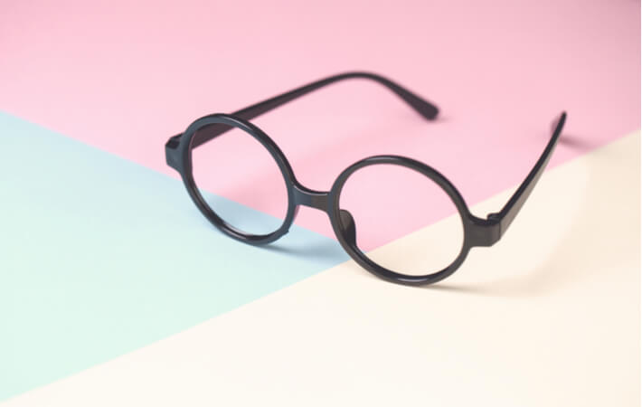 A black pair of glasses sits open upon a multicoloured surface.