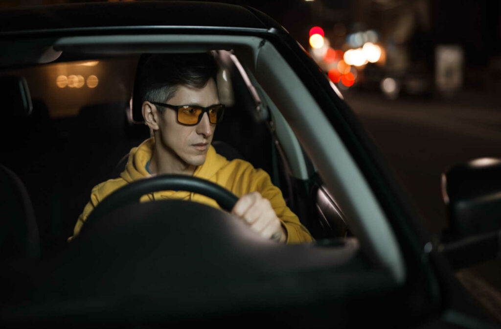 A man driving with blue light glasses checks his side mirror while driving.