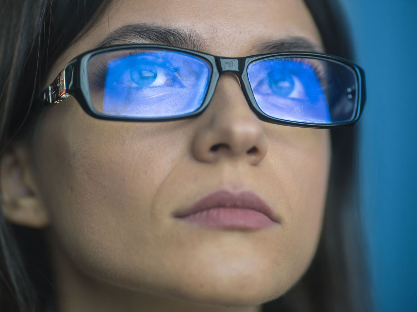 Photo of a woman's face with blue light reflecting off of her glasses.