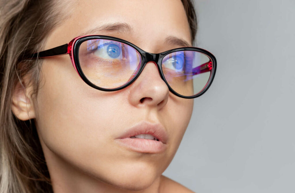 Close up of a woman's face showing blue light reflecting off of her glasses.